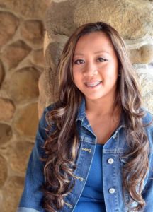 girl in jean jacket smiling leaning against stone wall