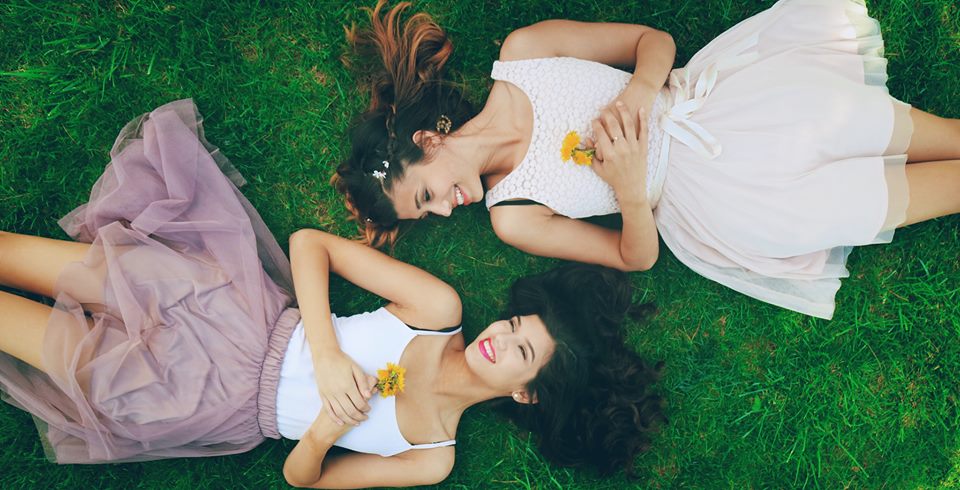 2 girls laying in the grass smiling holding flowers